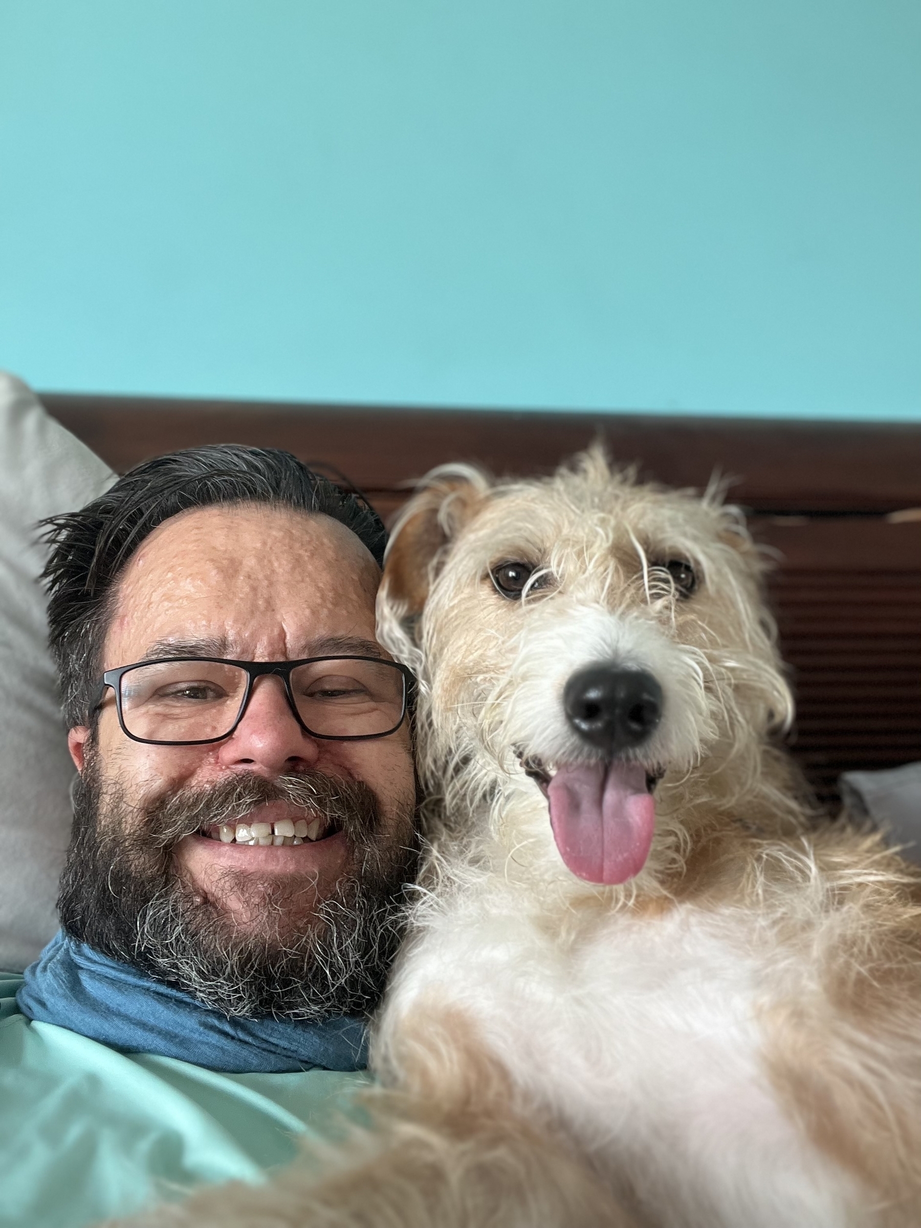 Beardy man smiles next to smiling lurcher. 