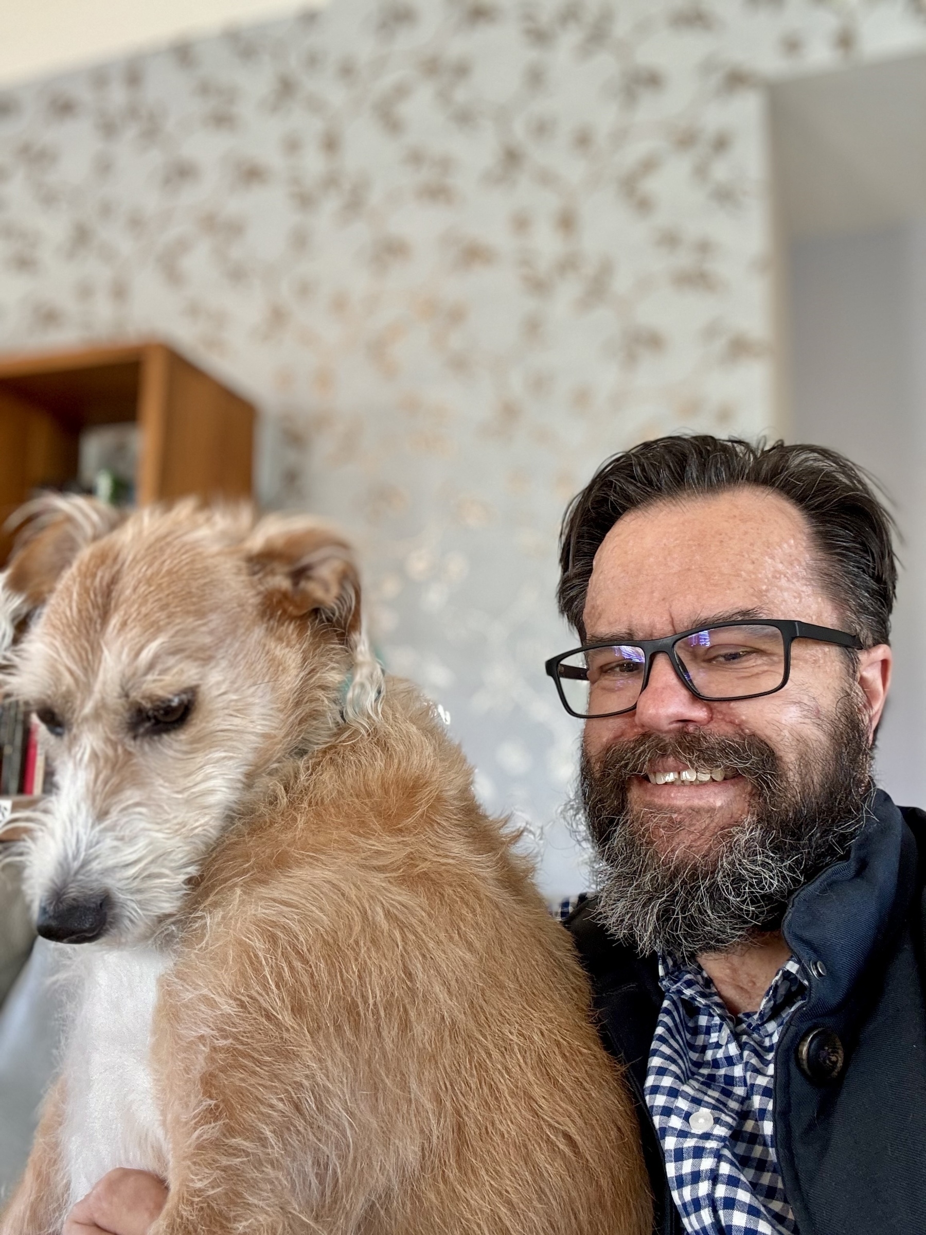 A hairy man hugs a bashful lurcher. 