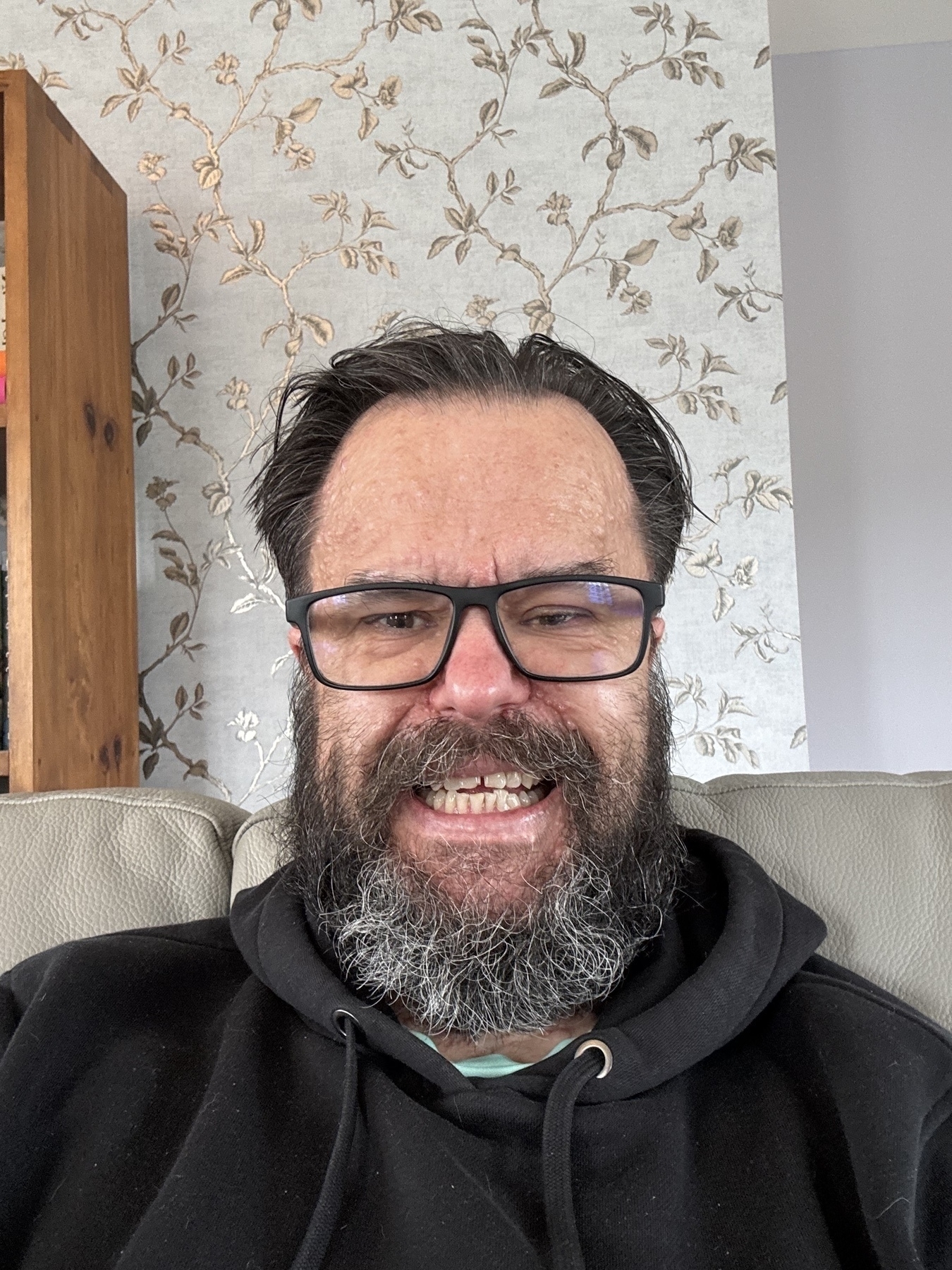 A hairy faced man with a winning smile grins in an awkward selfie. 